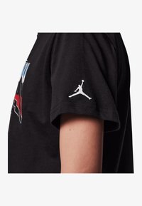Czarny bawełniany t-shirt z okrągłym dekoltem, z kolorowym nadrukiem graficznym oraz białym logiem Jumpman na lewym rękawie.