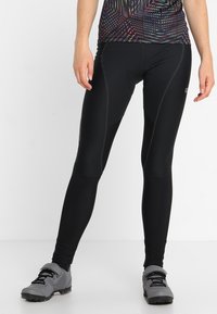 Svarta leggings med en åtsittande passform, tillverkade av elastiskt tyg, med platta sömmar och subtila designinslag. Kombineras med grå sportskor.