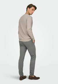 Pull beige texturé, pantalon gris slim et chaussures marron. Le pull présente un motif côtelé ; le pantalon est coupé pour une silhouette élégante.