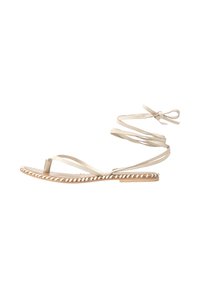 Beige sandal med stropper, tynde snore, flad sål og dekorative fletdetaljer langs kanten. Åben tå design.