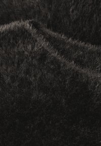Tessuto nero a trama con lunghe fibre morbide, caratterizzato da una leggera ondulazione sulla superficie che crea profondità e interesse visivo.