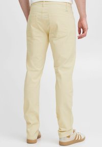Pantalones amarillo claro de algodón, con dos bolsillos traseros y un corte recto. Combinados con zapatillas beige.