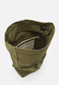 Olive green canvas backpack with a top opening, featuring an inner zipper pocket and two outer compartments with zip closures and straps.