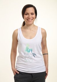 Hvid tanktop med et akvarel havfrue-design i grønt og blåt, ledsaget af teksten "havets ♥." Blødt stof, afslappet pasform.