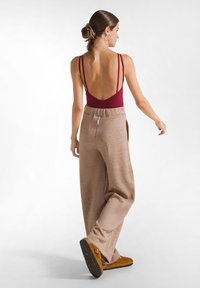 Bordeaux rugloze bodysuit met dunne bandjes, gecombineerd met losse, glinsterende beige broek en bruine schoeisel. Eenvoudig design met een zachte textuur.