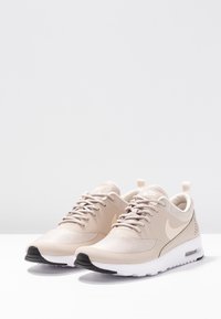 Béžové sportovní boty s horní částí z prodyšné síťoviny, kulatou špičkou, šněrováním a kontrastní černou gumovou podrážkou. Mají logo a poutko na patě.