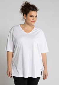 T-shirt bianco in cotone con scollo a V, maniche corte e spacchetti laterali. Vestibilità ampia con una texture liscia e un design semplice.