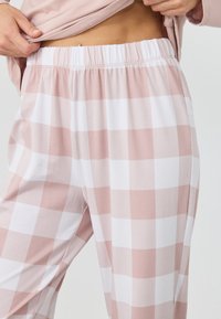 Lyserøde og hvide ternede pyjamabukser med elastisk talje, lavet af blødt stof med en glat tekstur.