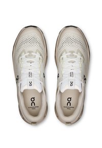 Lichtbeige hardloopschoenen met een bovenkant van mesh, textuurdetails, witte veters en rubberen zolen. Zwart logo en "Cloudsurfer Trail" branding zichtbaar.
