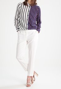 Pasiasta koszula z guzikami w granatowo-białym kolorze, z kontrastowym czerwonym paskiem. Połączona z białymi spodniami i połyskującymi różowozłotymi obcasami.