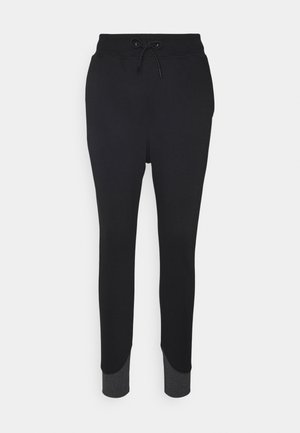 Pantalon de jogging noir avec taille à cordon de serrage et poignets côtelés gris foncé sur un fond clair uni.