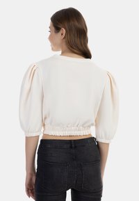 Krátký rukáv, zkrácený vršek ze měkké krémové tkaniny, s nařasenými rukávy a elastickým pasem. V kombinaci s tmavými slim-fit džíny.