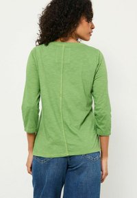 Green, lightweight long-sleeve top with a rounded neckline and three-quarter sleeves. Features a central seam on the back. Casual fit; soft texture.