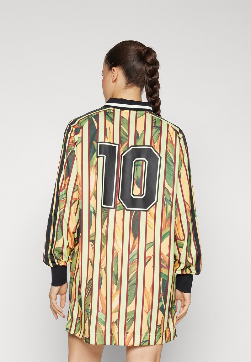 Maillot de sport à manches courtes avec un motif rayé jaune et vert et des accents de feuilles. Porte le numéro "10" en noir au dos.