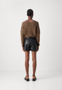Brun strikket sweater med en afslappet pasform, parret med sorte lædershorts med en glat tekstur og oprevet kant. Glatte sorte sko.