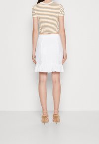 Pruhovaný krátký top v béžové a bílé barvě, zkombinovaný s bílou sukní s očkovým vzorem a volánkovým lemem. Model nosí nahé sandály na vysokém podpatku.