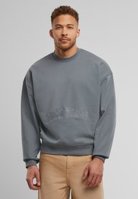 Grå genser med rund hals, oversized passform, med brodert "Trust Issues"-tekst på fronten, laget av myk bomullsmateriale.