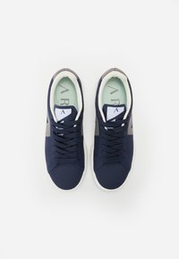 Zapatillas de malla azul marino con acentos grises, suela blanca y cordones tonales. Cuenta con una plantilla verde clara con un patrón de logo. Textura suave.