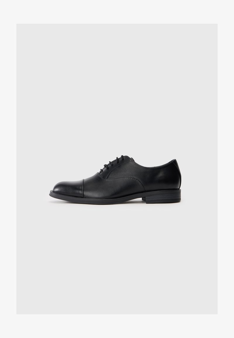 Musta nahast kontsaking, ümarate varvastega, nööpimisega disain, sile pind ja madal, tasane konts. Minimalistlik esteetika, ilma nähtava brändita.