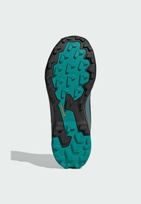 Trailrunning-Schuhsohle mit einer schwarzen Außenschicht und einer strukturierten tealfarbenen Gummibasis mit multidirektionalen Stollen für Traktion.