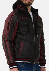 Schwarze und burgunderrote Bomberjacke mit strukturiertem Finish, Reißverschlusstaschen, gestreiften Bündchen und einer schwarzen Kapuze. Mit Branding auf der Schulter.