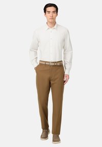 Camicetta bianca a righe con bottoni, pantaloni marroni a gamba stretta, cintura intrecciata beige e sneaker beige. Design minimalista con una texture liscia.