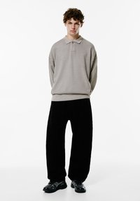 Világosszürke, oversized polo pulóver bordázott textúrával és gallérral, fekete, széles szárú nadrággal és fényes fekete cipővel párosítva.