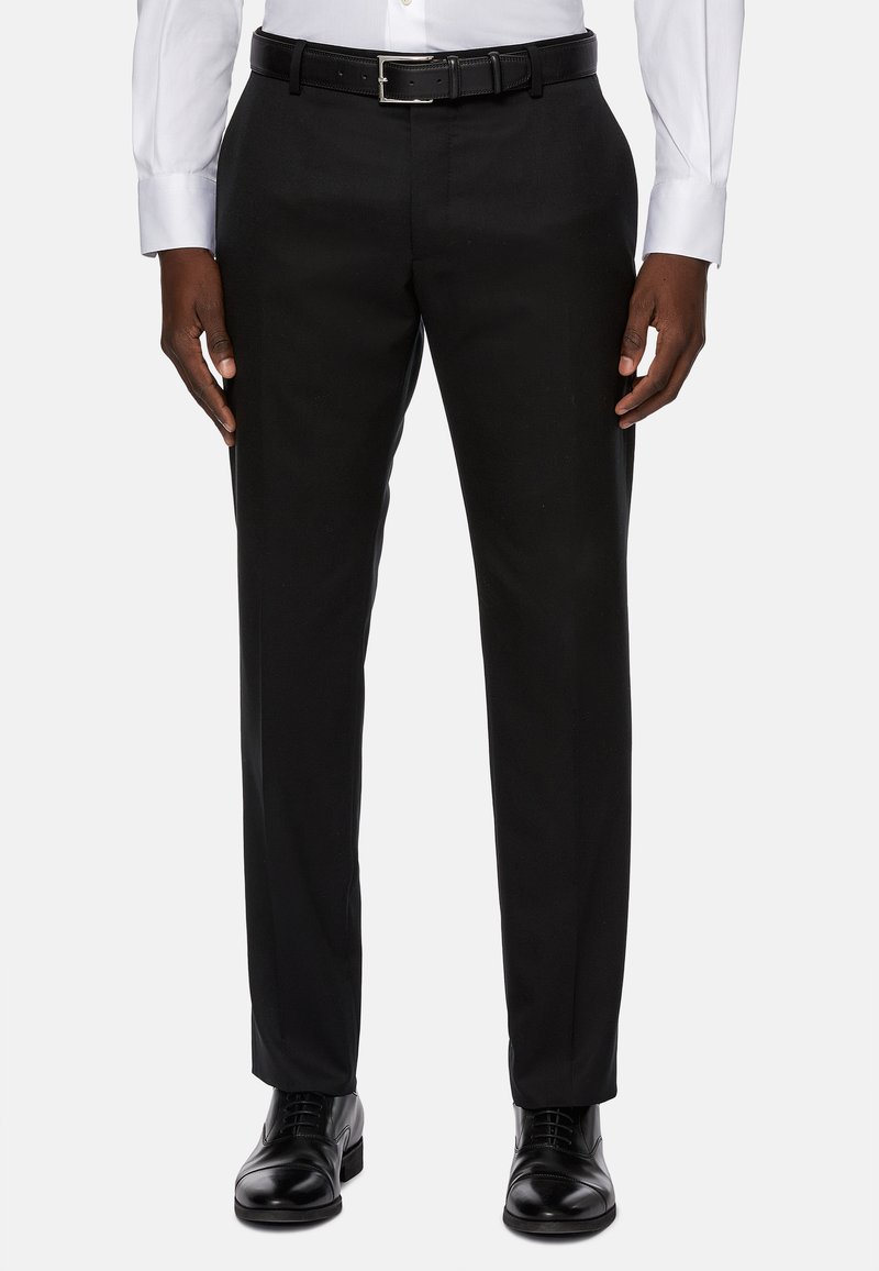 Črne hlače v ravnem kroju, izdelane iz gladkega materiala, z pregibi spredaj in klasičnim črnim pasom v kombinaciji s sijočimi čevlji.