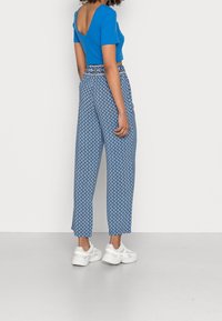 Modrý crop top s vykrojeným zadním dílem, kombinovaný s modrými širokými kalhotami s geometrickým vzorem a kontrastním pasem. Bílé tenisky.