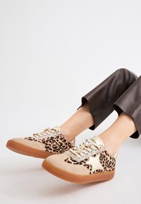 Zapatos de estampado de leopardo con parte superior de ante beige y metálico, adornados con un acento brillante. Suela de goma y cordones de tela.