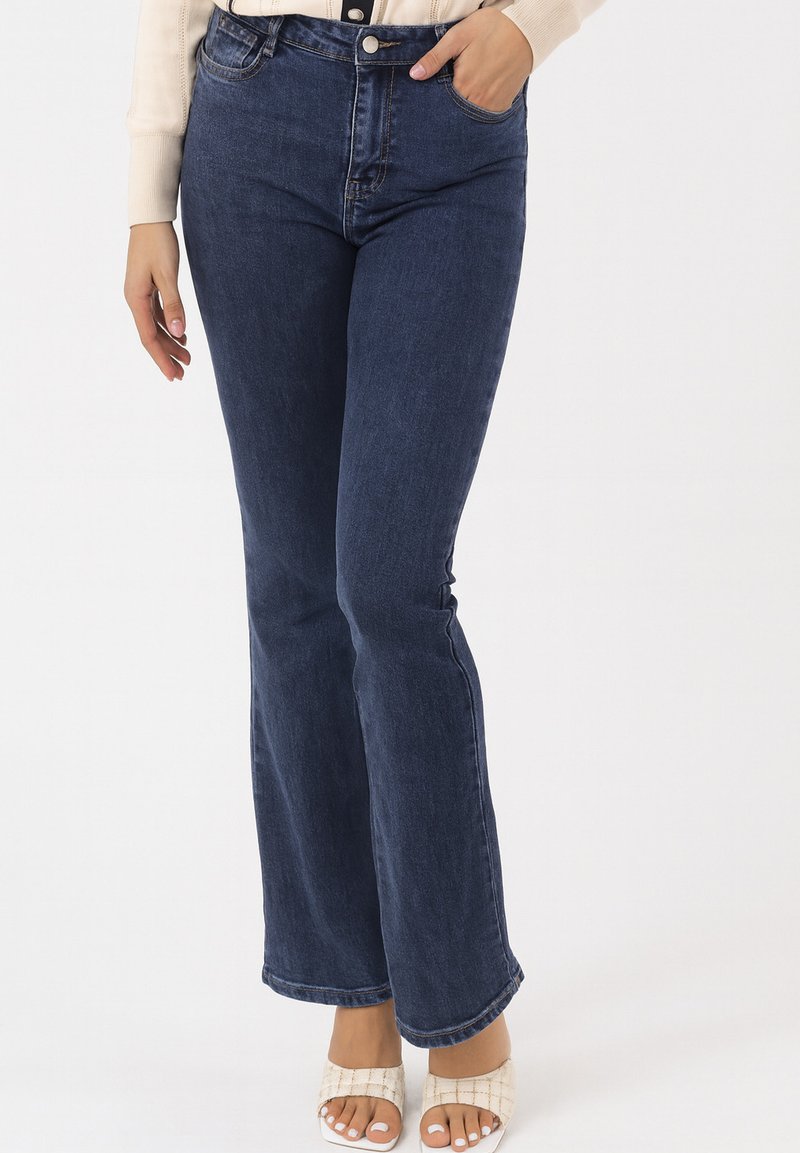 Pantalones vaqueros acampanados de color azul oscuro hechos de mezclilla, con cintura alta, cierre frontal con botones y diseño clásico de cinco bolsillos. Textura suave en toda la prenda.