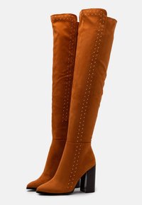 Stivali over-the-knee in suede arancione con punta a punta, tacco a blocco e file verticali di borchie argentate lungo i lati esterni.