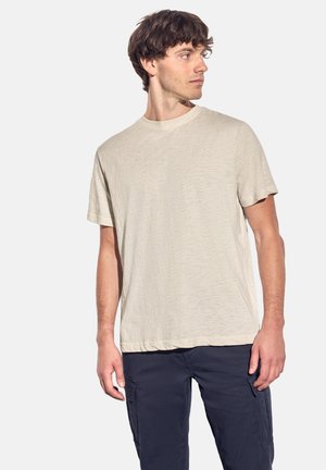 Helles beiges Baumwoll-T-Shirt mit Rundhalsausschnitt und kurzen Ärmeln sowie einer subtilen Struktur, kombiniert mit dunkelblauen Cargo-Hosen.