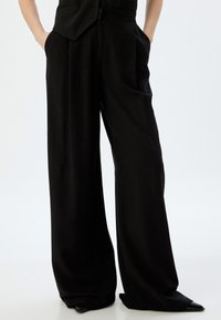 Schwarze weit geschnittene Hose aus glattem Stoff mit hoher Taille, seitlichen Taschen und einem lässigen Schnitt, der am Knöchel schmaler zuläuft.
