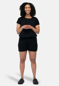 Zwart geribbeld T-shirt met korte mouwen in combinatie met zwarte shorts. De outfit heeft een losse pasvorm en wordt gedragen met donkere instappers.