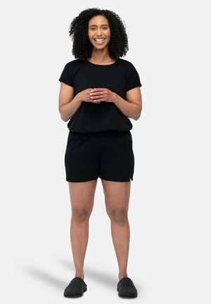 Top corto a maniche corte a righe nere abbinato a pantaloni corti neri. L'outfit presenta una vestibilità comoda ed è completato da scarpe slip-on scure.
