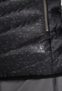 Svart puffjacka med mönstrad textur, horisontell quiltad design och silverdragkedja. Har logotypen "Jack Wolfskin" i vitt.