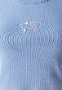 Haut en tissu côtelé bleu clair brodé de texte blanc « From Another Planet » avec un petit dessin de planète et d'orbite.
