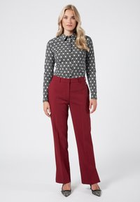 Czarna i biała wzorzysta koszula z długim rękawem połączona z dopasowanymi burgundowymi spodniami. Spodnie mają gładką teksturę i lekki połysk. Szpiczaste czarne obcasy.