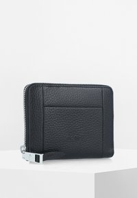 Cartera de cuero negra con una superficie texturada, que cuenta con un cierre de cremallera, una correa lateral y un logotipo en relieve en la parte frontal.