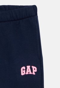 Navy blue sweatpants made of soft fabric, featuring an elastic waistband and a pink "GAP" logo embroidered on the side.