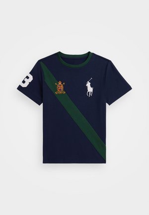 T-shirt en coton marine avec une bande diagonale verte, un logo de polo blanc, un blason brodé et le chiffre '3' blanc sur la manche gauche.