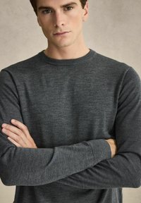 Mörkgrå stickad tröja med rund halsringning och långa ärmar. Tyget verkar mjukt med en subtil textur. Inkluderar ribbade ärmslut och nederkant.