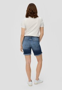 Dżinsowe szorty w średnim niebieskim odcieniu, z podwiniętymi rękawami, pięciokieszeniowy fason, w zestawie z prostą białą koszulką z krótkim rękawem i białymi butami.