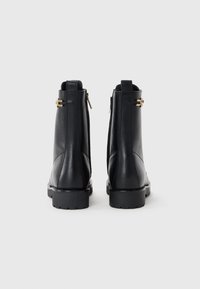 Black leather ankle boots with a textured finish, featuring two side zippers, and a chunky rubber sole. Gold hardware accents visible.