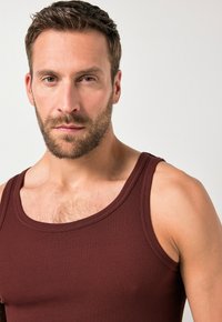 Top de tirantes acanalados burdeos con tirantes anchos, que presenta una tela texturizada y un diseño ajustado, que resalta el pecho y los hombros.
