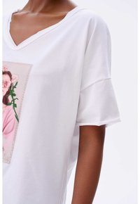 Witte T-shirt met korte mouwen en een V-hals, voorzien van een bloemig grafisch ontwerp dat centraal op de voorkant staat. Zacht materiaal met een relaxte pasvorm.