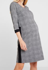 Svart och vit rutig klänning med trekvartsärmar, rund halsringning och svarta sidopaneler. Mjuk tygkvalitet och avslappnad passform.