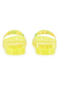 Κίτρινα σανδάλια ζελέ με δύο διαφανείς λουράκια. Η σόλα έχει λαμπερή υφή, με έντονα γράμματα στο μπροστινό λουράκι  σε διάφορα χρώματα.