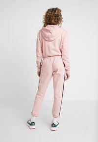 Rosa huva sweatshirt med elastisk midja och matchande sweatpants med svarta sidostråk. Modellen bär färgglada sneakers.
